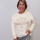 Woman wearing a cream sweatshirt with decorative elements against a white wall