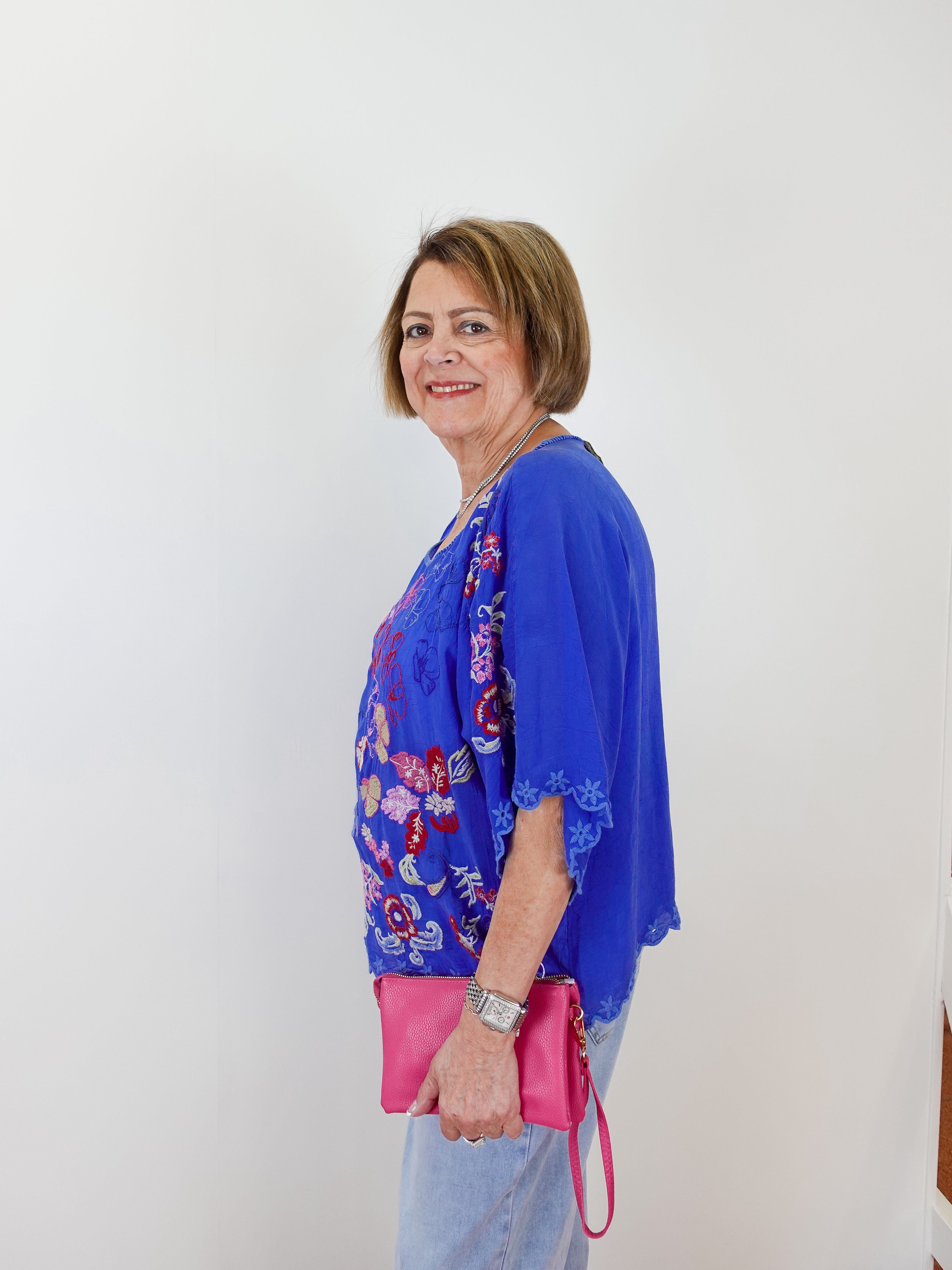 Woman wearing a blue floral blouse and holding a pink bag against a white background