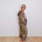 Person wearing a leopard print outfit with a scarf, standing against a white wall.