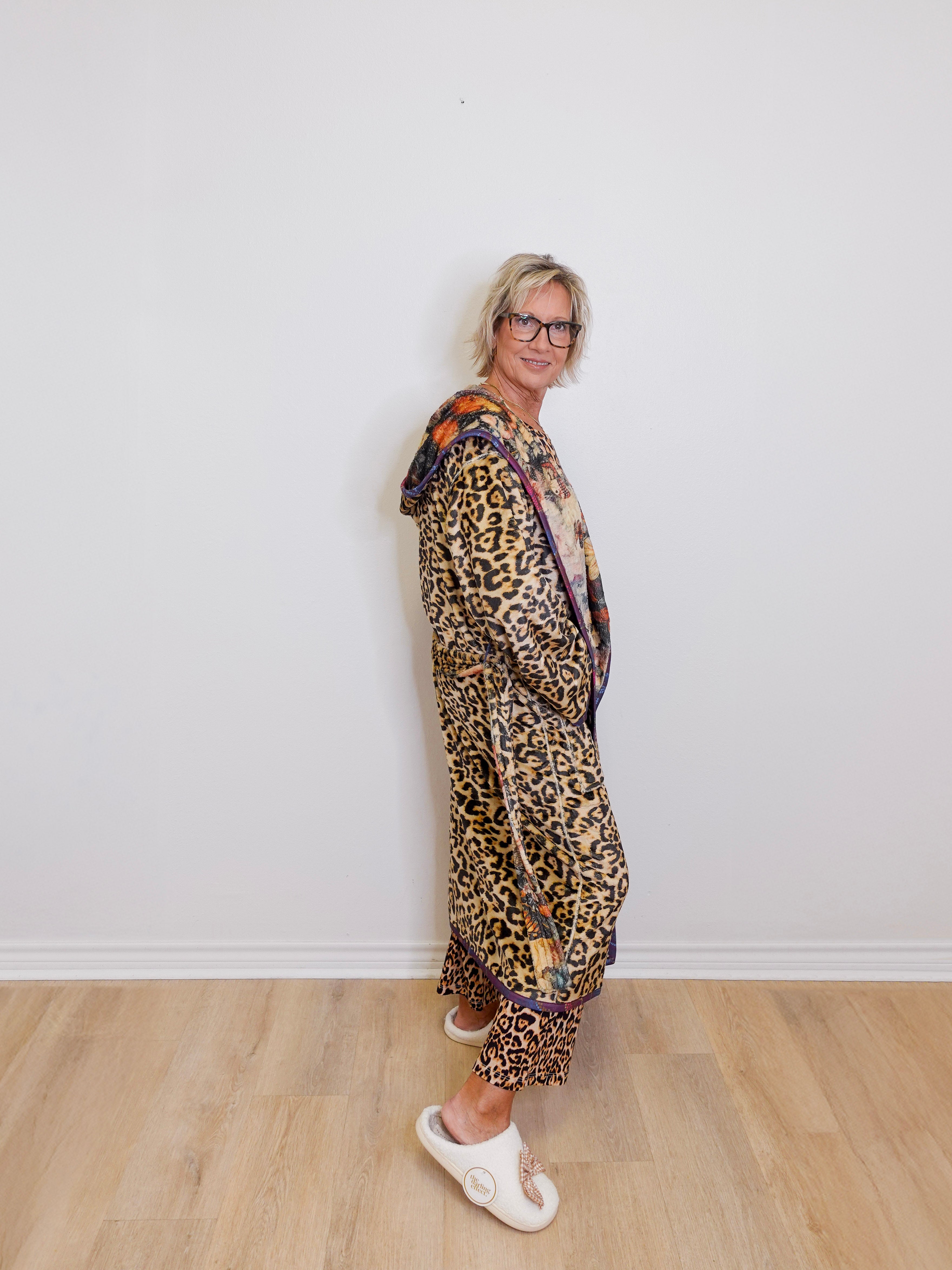 Person wearing a leopard print outfit with a scarf, standing against a white wall.