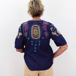 Person wearing a dark blue embroidered shirt with colorful patterns on a white background