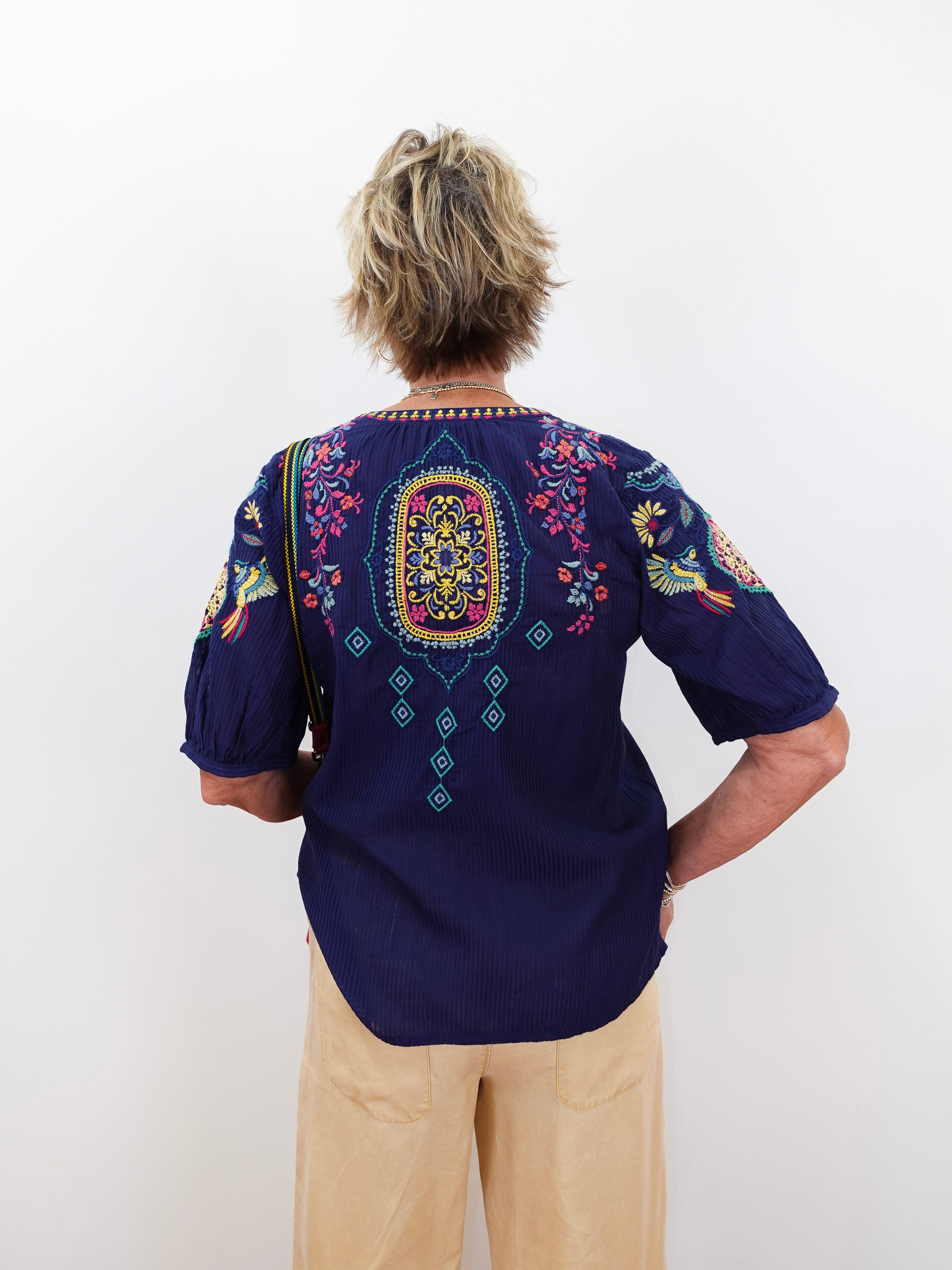 Person wearing a dark blue embroidered shirt with colorful patterns on a white background