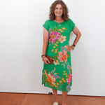 Woman wearing a green floral dress against a white wall.