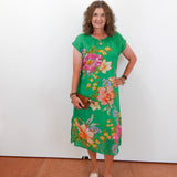 Woman wearing a green floral dress against a white wall.