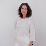 Woman wearing a white lace top and pants against a plain background