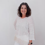 Woman wearing a white lace top and pants against a plain background