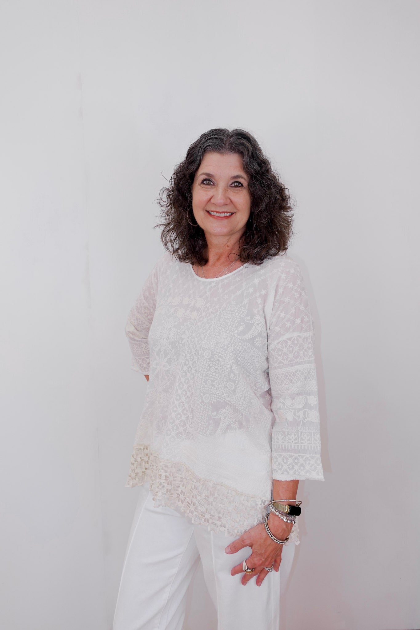 Woman wearing a white lace top and pants against a plain background