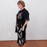 Woman wearing a black floral dress against a white wall.