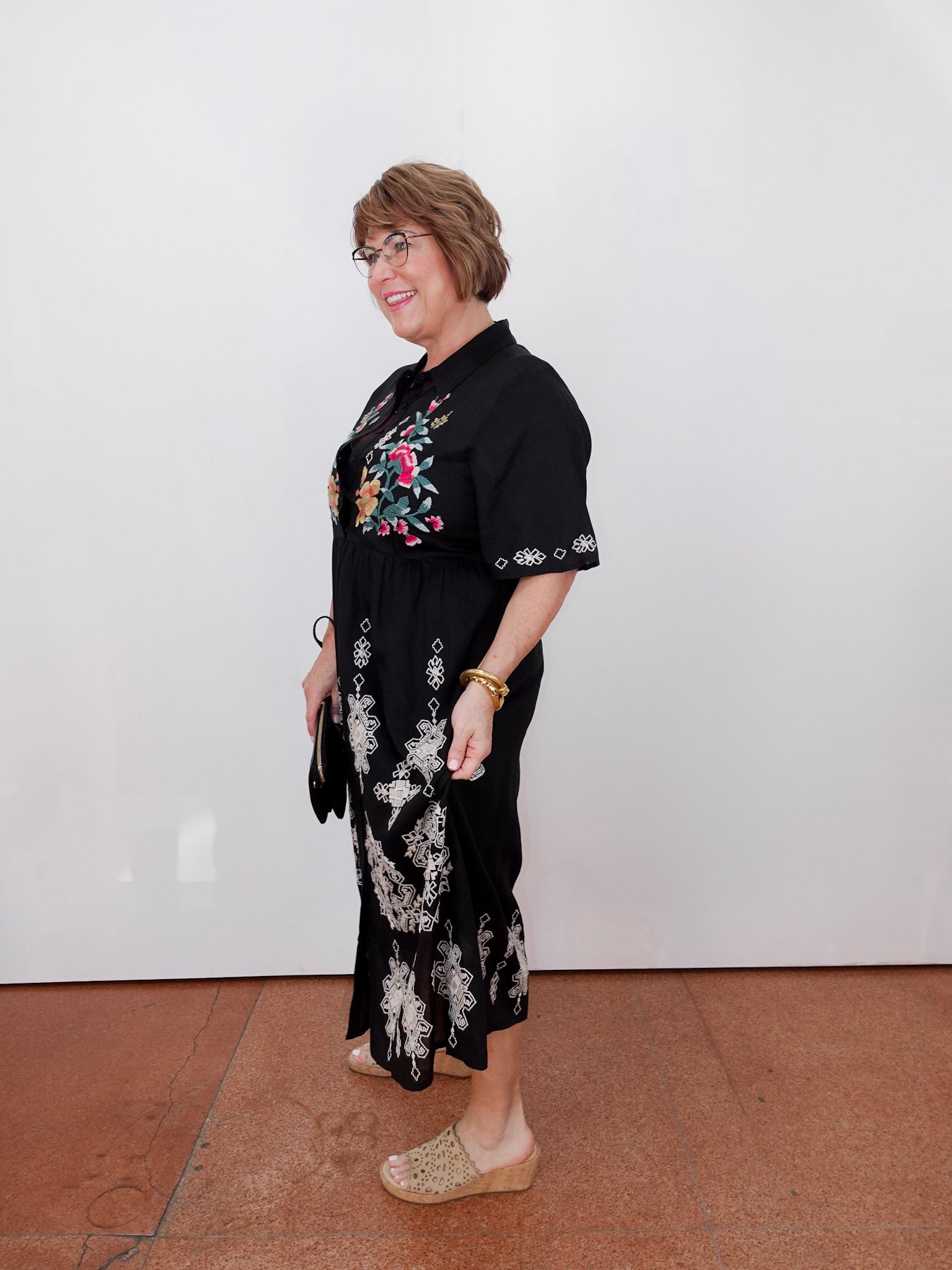 Woman wearing a black floral dress against a white wall.
