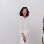 Woman in a white outfit standing against a plain white wall.