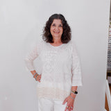 Woman in a white outfit standing against a plain white wall.