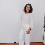 Woman wearing a white outfit standing against a plain white wall.