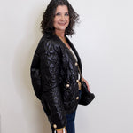 Woman wearing a black quilted jacket against a white wall