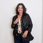 Woman wearing a black quilted jacket with gold buttons against a white background