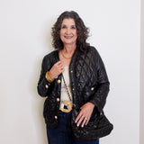 Woman wearing a black quilted jacket with gold buttons against a white background