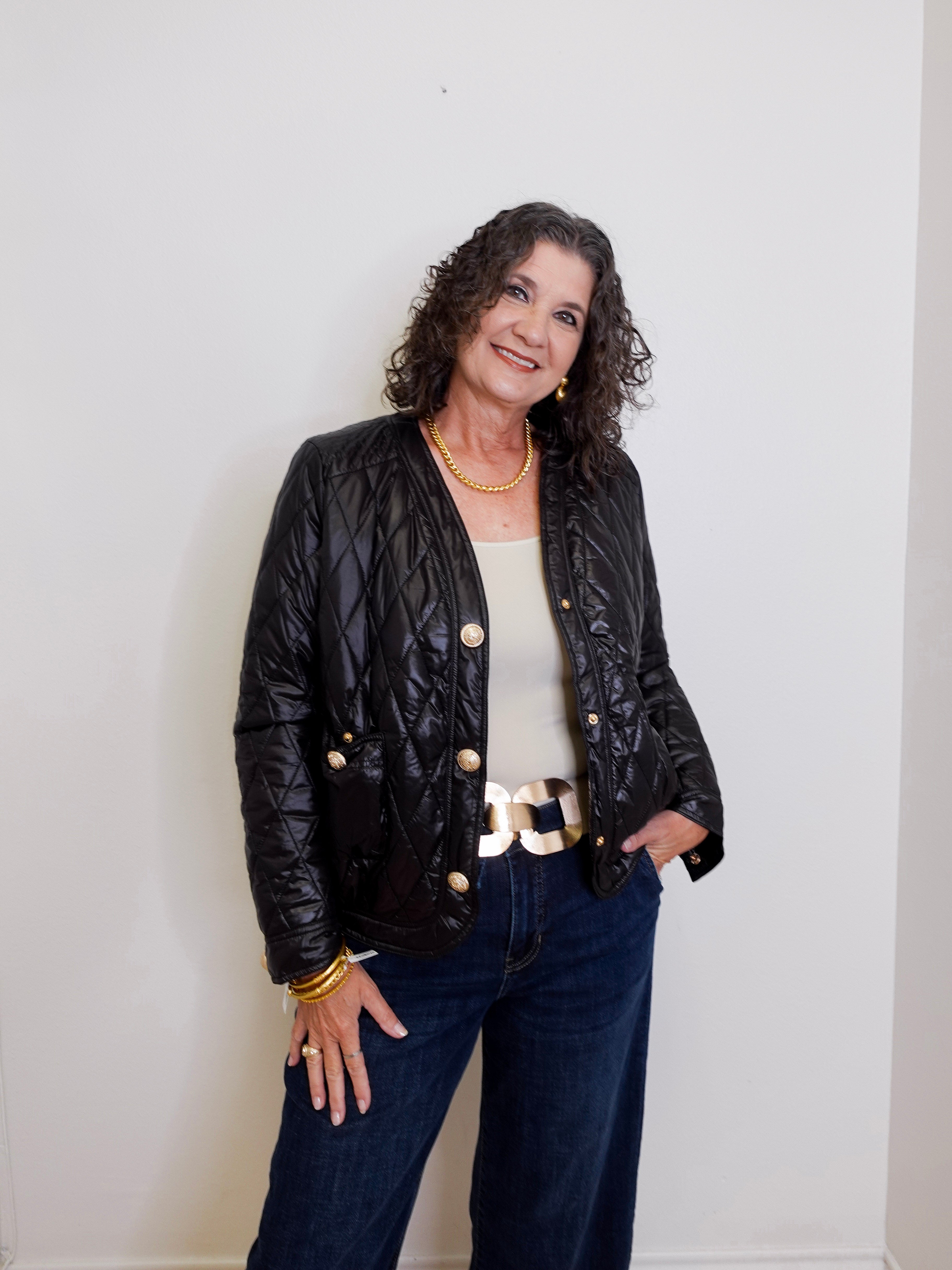 Woman wearing a black quilted jacket with gold buttons against a white background