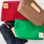 Four fabric pouches in red, green, black with leopard print, and beige on a white surface.