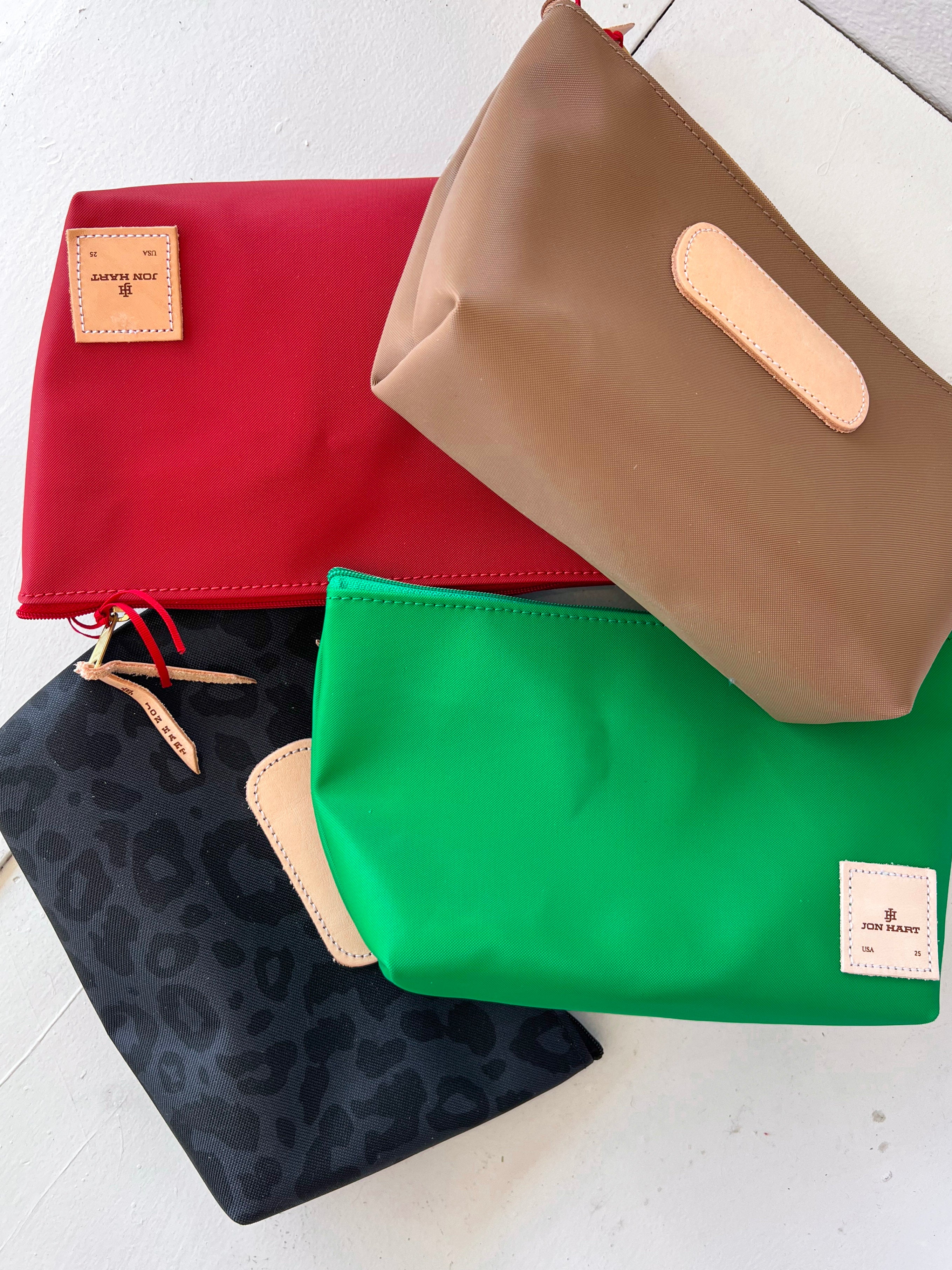 Four fabric pouches in red, green, black with leopard print, and beige on a white surface.