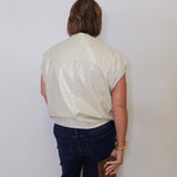 Person wearing a light-colored shirt and dark pants against a plain background
