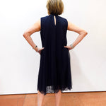 Woman modeling a Joseph Ribkoff high neck A-line dress featuring a sleeveless silhouette, pleated fabric, and floral accent detail.