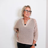 Woman wearing a patterned sweater and black pants against a white background