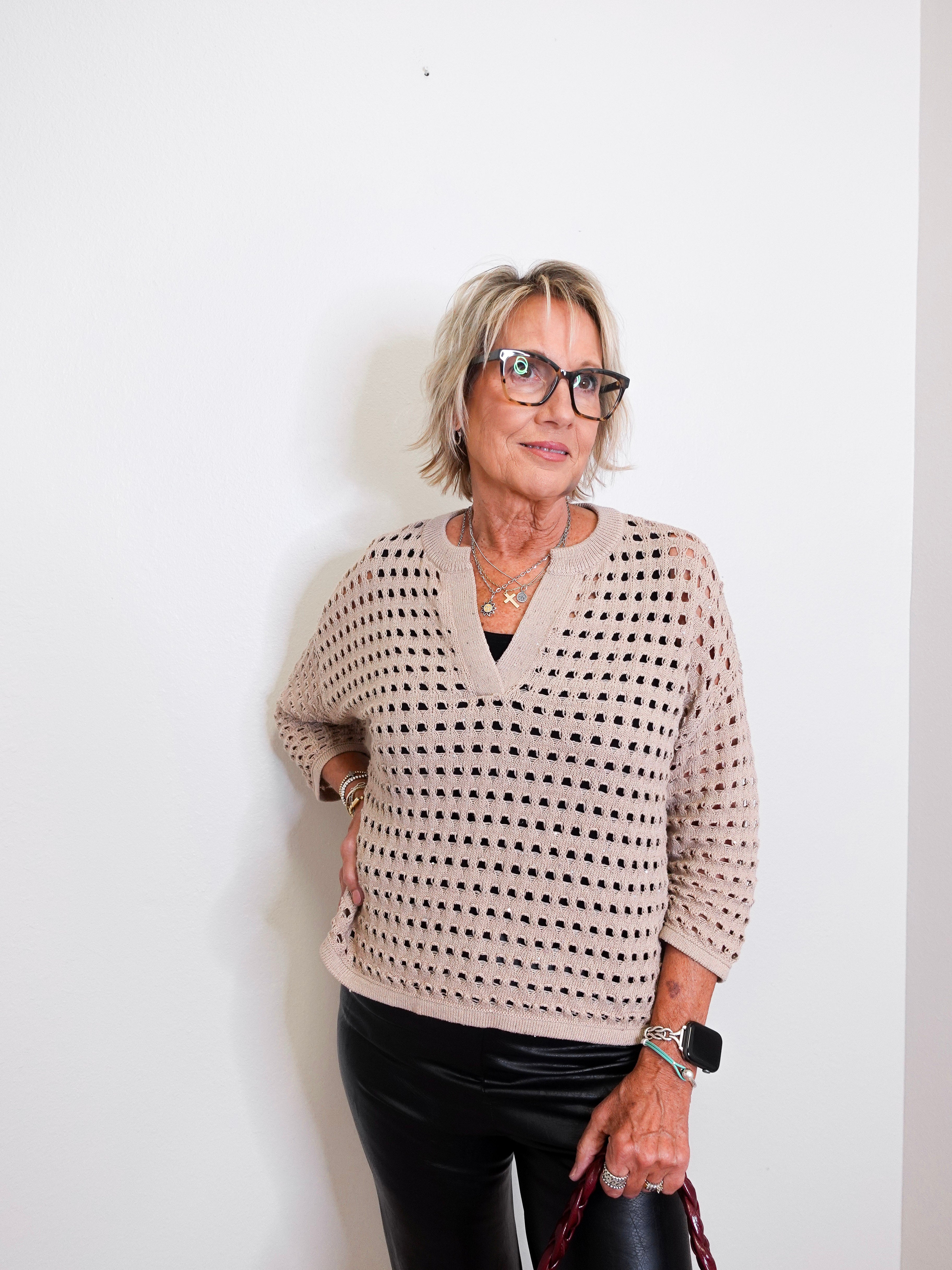 Woman wearing a patterned sweater and black pants against a white background