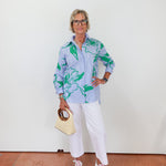 Woman wearing a light blue floral shirt with white pants, holding a beige handbag.