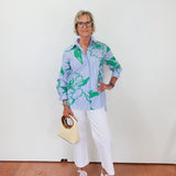 Woman wearing a light blue floral shirt with white pants, holding a beige handbag.