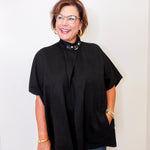 Woman wearing a black poncho and glasses against a white background