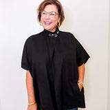 Woman wearing a black poncho and glasses against a white background