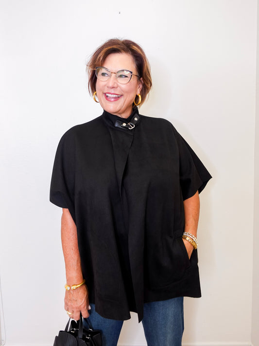 Woman wearing a black poncho and glasses against a white background