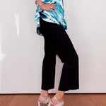 Person wearing a blue and white patterned top with black pants and white sandals on a plain background