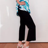 Person wearing a blue and white patterned top with black pants and white sandals on a plain background