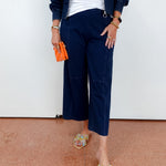 Person wearing navy outfit with white top and colorful sandals on a plain background