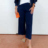 Person wearing navy outfit with white top and colorful sandals on a plain background