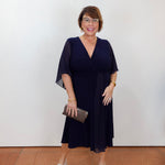 Model wearing a Joseph Ribkoff fit and flare dress in navy with a v-neckline and flowy short sleeves.