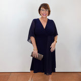 Model wearing a Joseph Ribkoff fit and flare dress in navy with a v-neckline and flowy short sleeves.