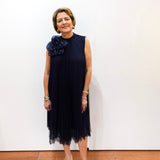 Model wearing a Joseph Ribkoff high neck A-line dress in navy with pleated fabric and floral appliqué detail.