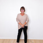 A woman wearing a v-neck jewel embellished sweater and black pants in front of a white wall.