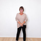 A woman wearing a v-neck jewel embellished sweater and black pants in front of a white wall.