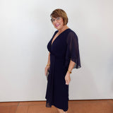 Woman modeling a Joseph Ribkoff fit and flare dress featuring a navy silhouette, flattering v-neck, and flowy sleeves.