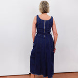 Person wearing a blue dress standing against a white wall.
