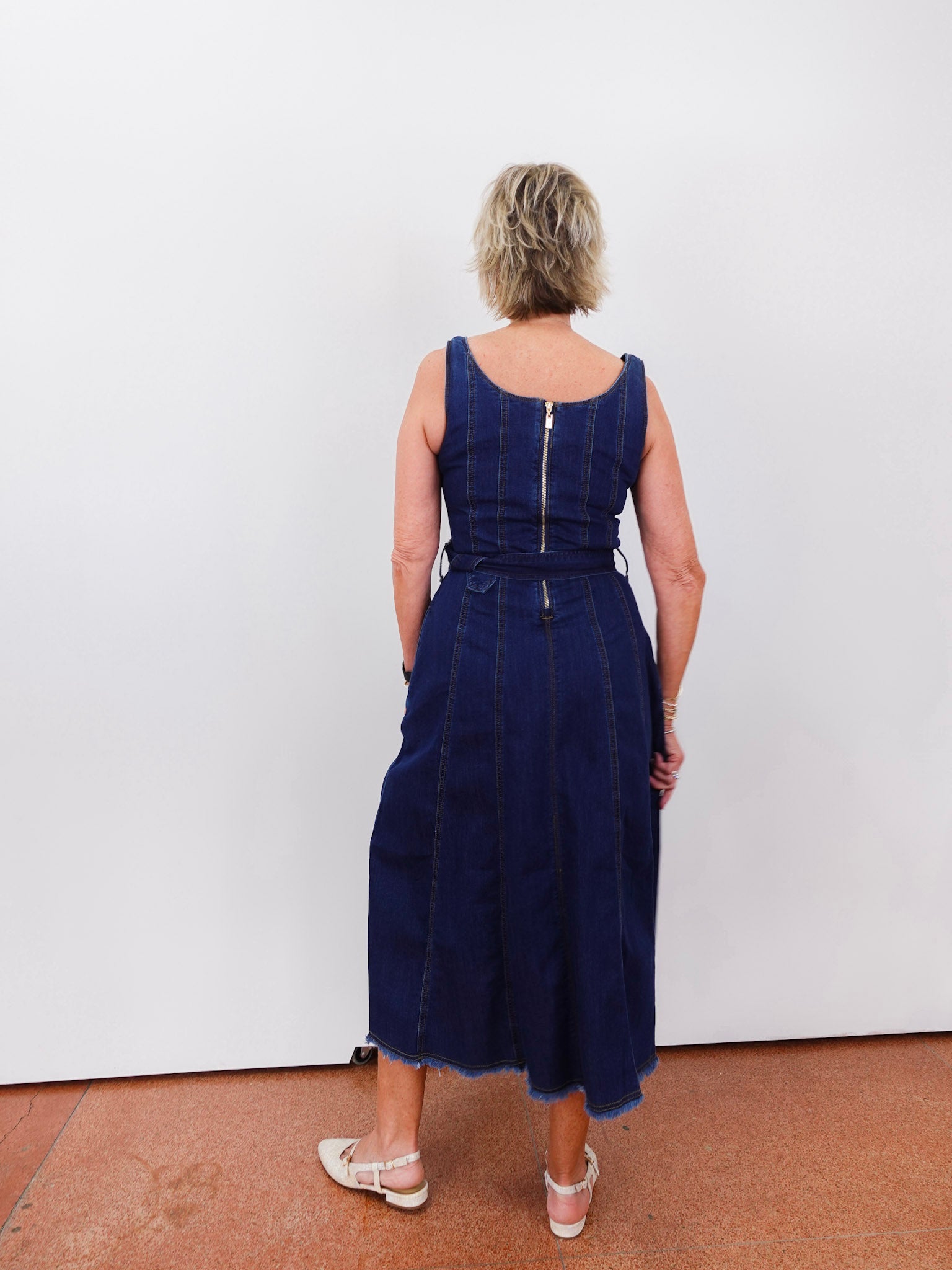 Person wearing a blue dress standing against a white wall.