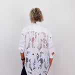 Person wearing a white shirt with black and brown pattern against a plain background