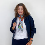 Woman wearing a colorful scarf, white shirt, and navy jacket against a plain background