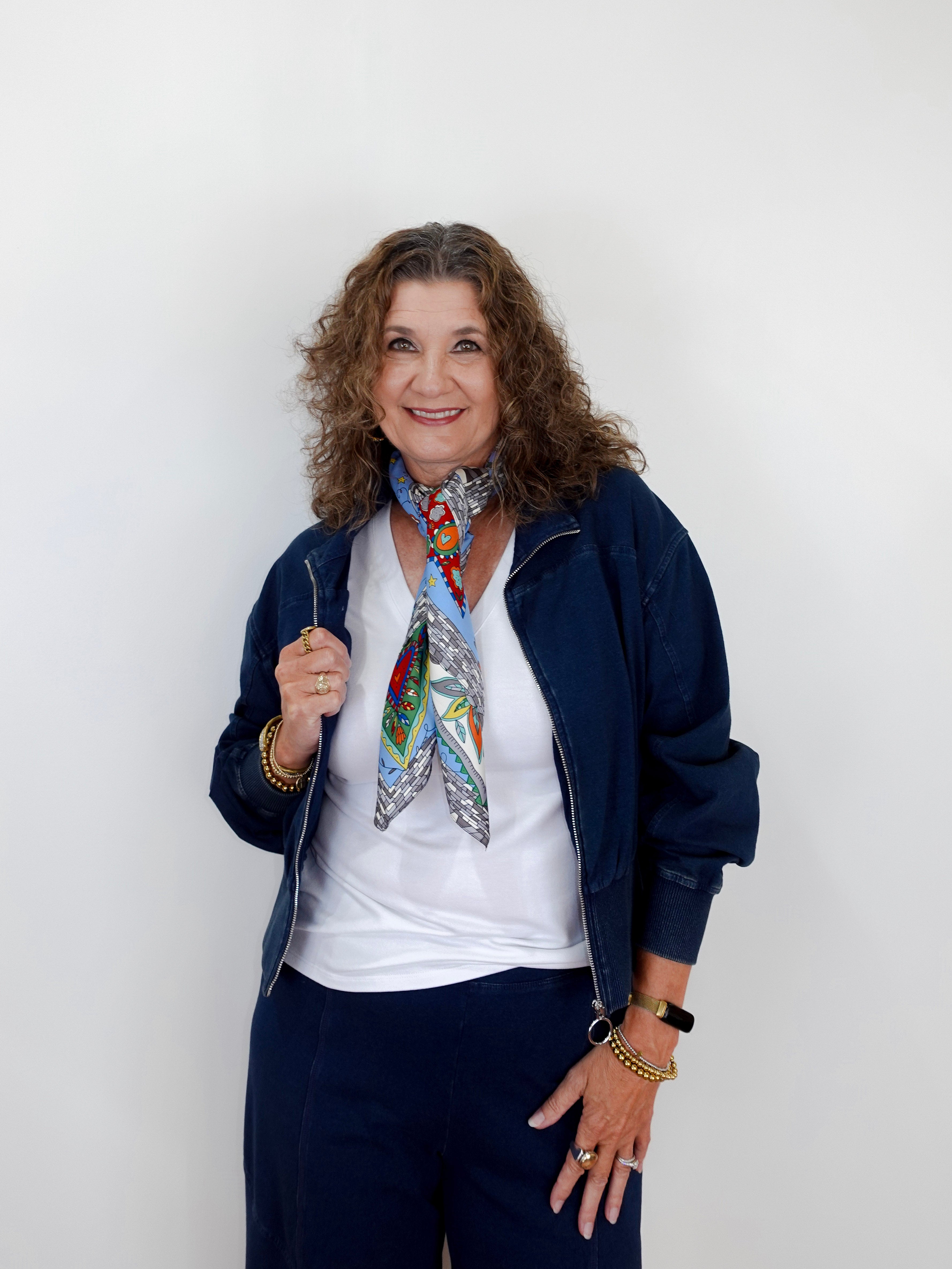 Woman wearing a colorful scarf, white shirt, and navy jacket against a plain background