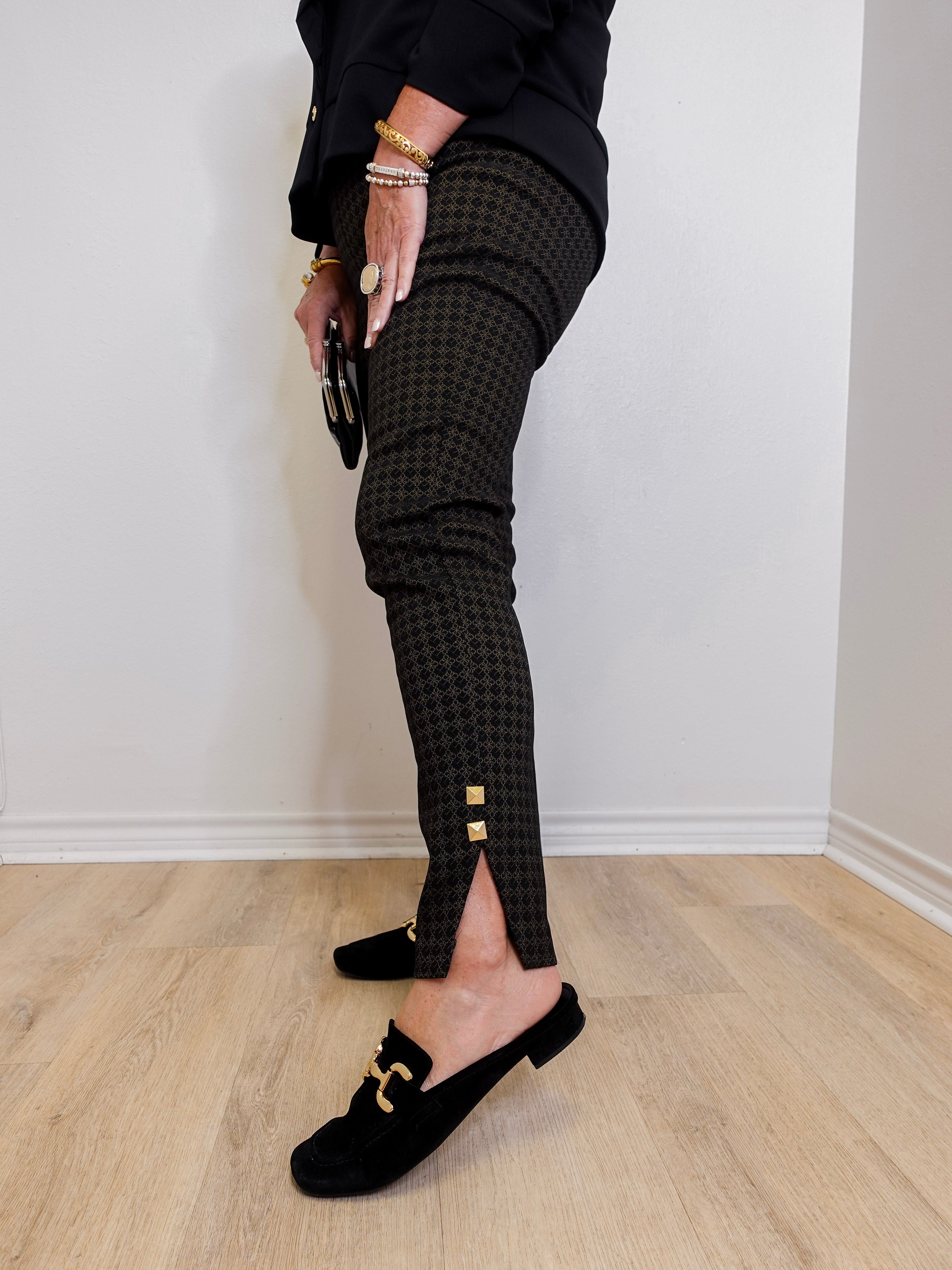 Person wearing black checkered pants with gold buttons and black loafers on a light wooden floor.