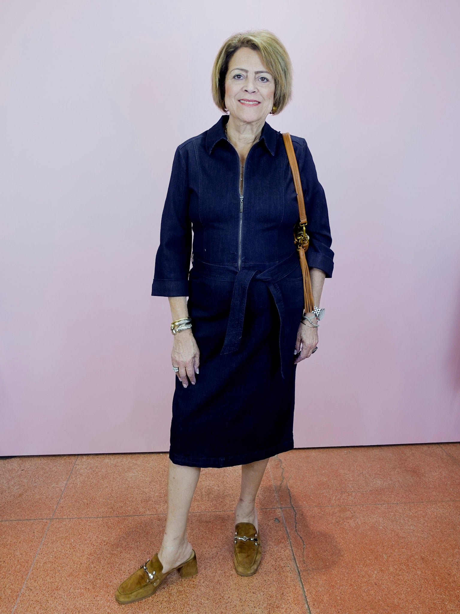 Woman wearing a navy dress with a brown bag against a pink wall.