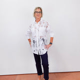 Person wearing a white floral shirt and dark pants against a white wall.