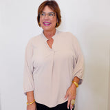 Woman wearing a beige blouse and black pants against a white wall